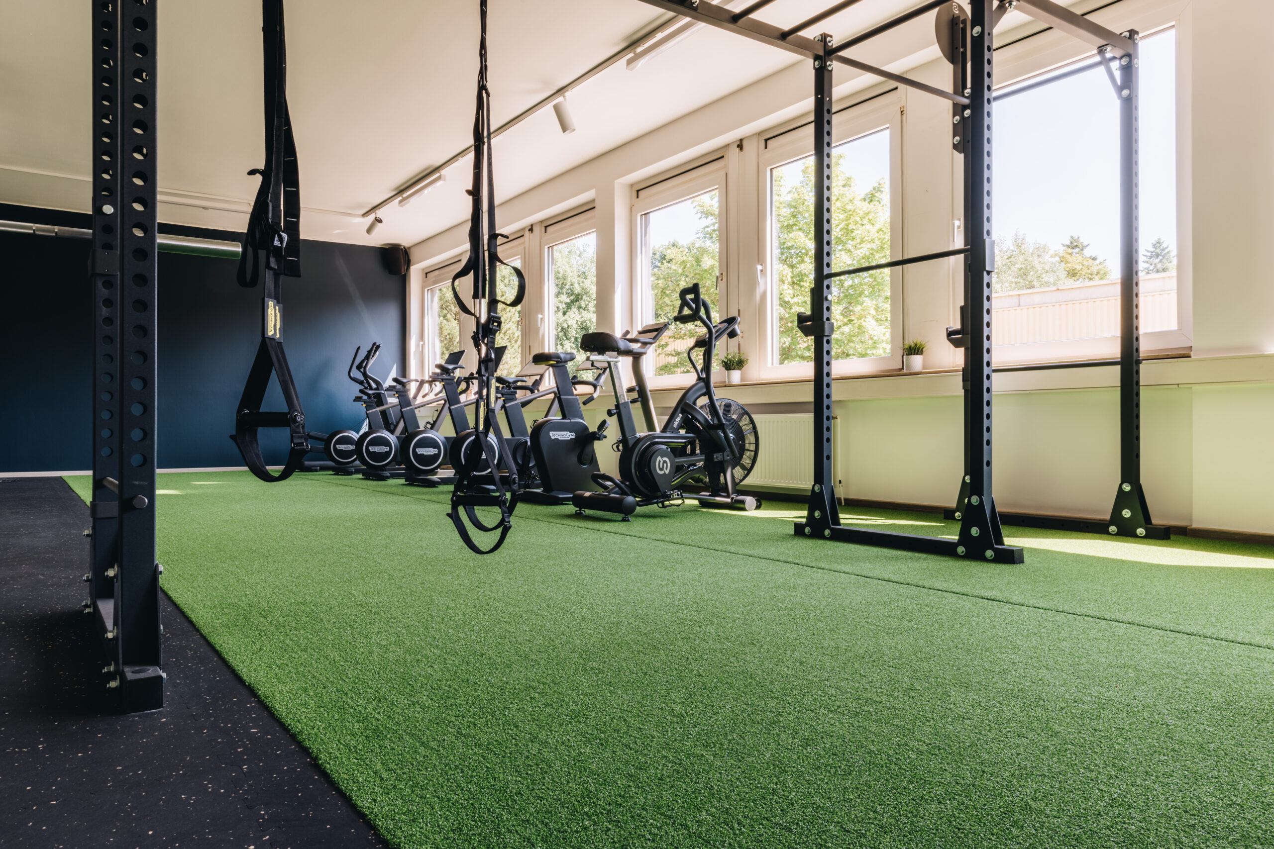 Sportstudio Norderstedt Cardio Bereich Im Vordergrund ist ein Rack zu sehen, für Klimmzüge und TRX und im Hintergrund die Fahrräder und Crosstrainer aus dem Cardio Bereich.
